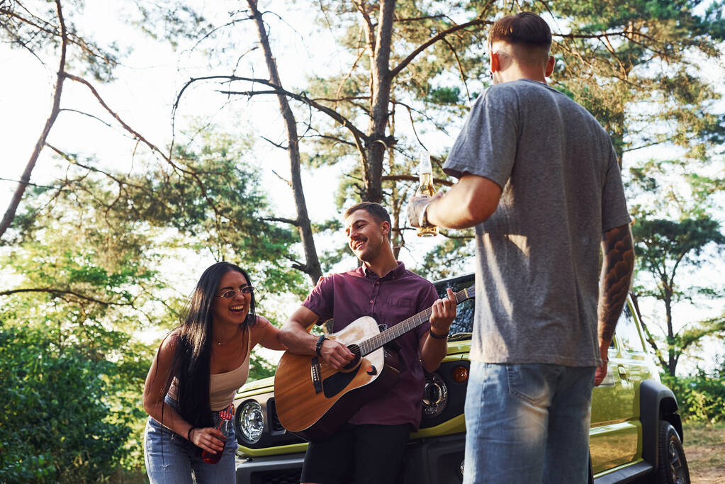 Chantons ensemble. Les amis ont beau week-end en plein air près de leur voiture verte avec guitare acoustique. - Photo, image