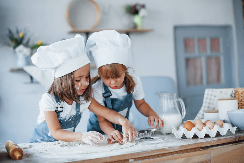 Концентрується на приготуванні. Сімейні діти в уніформі білого шеф-кухаря готують їжу на кухні
. - Фото, зображення