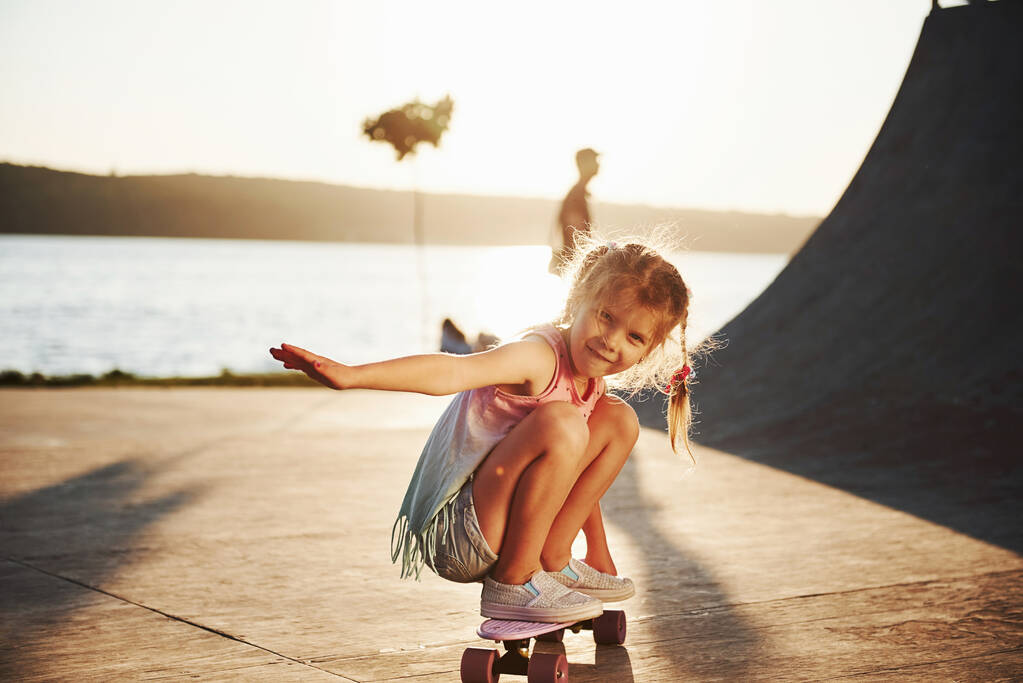 Pierwsze próby. Słoneczny dzień. Dzieciak bawi się na łyżwach na rampie. Wesoła dziewczynka.. - Zdjęcie, obraz
