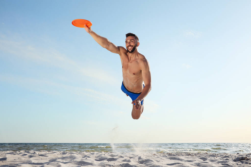 Hombre deportivo saltando y la captura de disco volador en la playa - Foto, Imagen