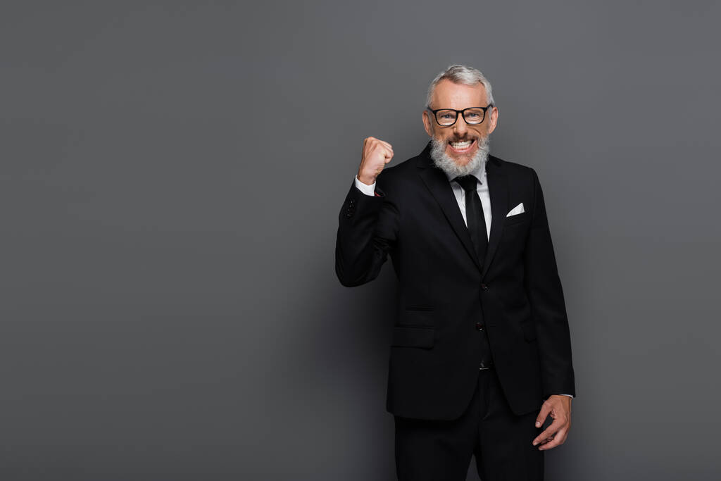 Aufgeregter Geschäftsmann mittleren Alters mit Brille jubelt vereinzelt auf grau - Foto, Bild