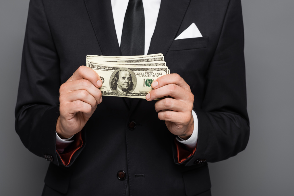 vista recortada del empresario de mediana edad sosteniendo billetes de dólar aislados en gris - Foto, imagen