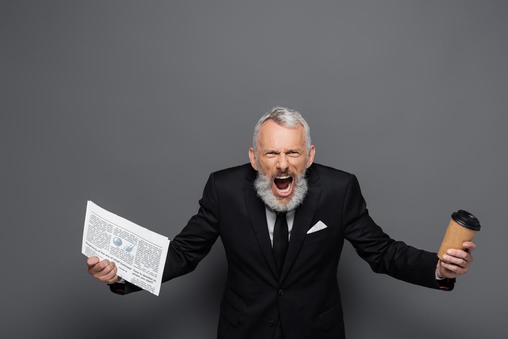 wütender Geschäftsmann mittleren Alters hält Pappbecher und Zeitung in der Hand, während er auf grau schreit - Foto, Bild