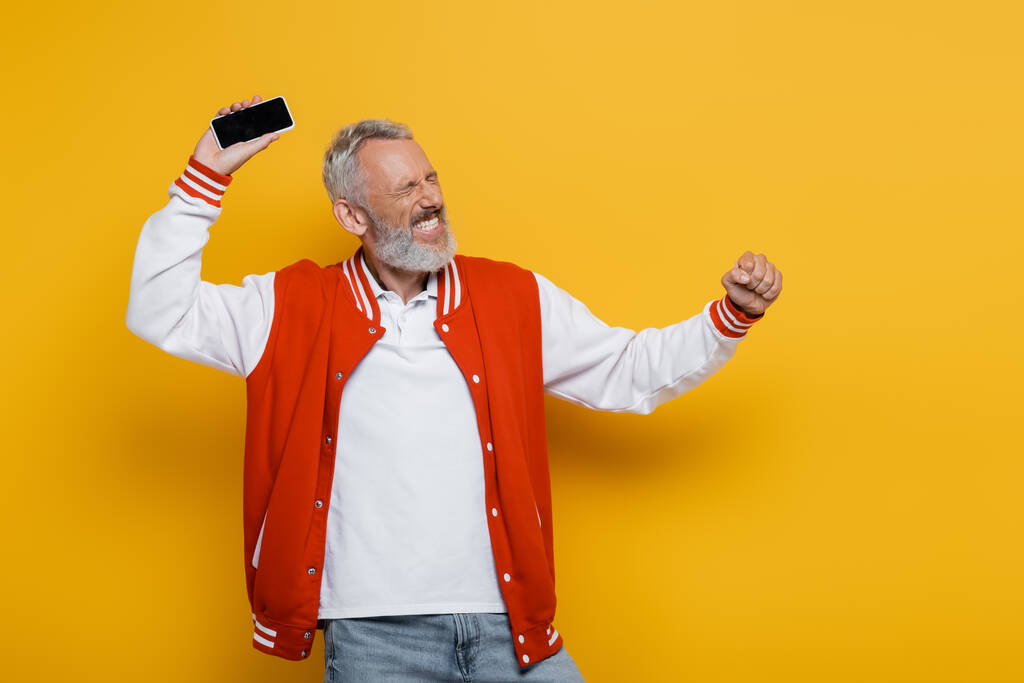 щасливий чоловік середнього віку з закритими очима тримає мобільний телефон з порожнім екраном на жовтому
  - Фото, зображення