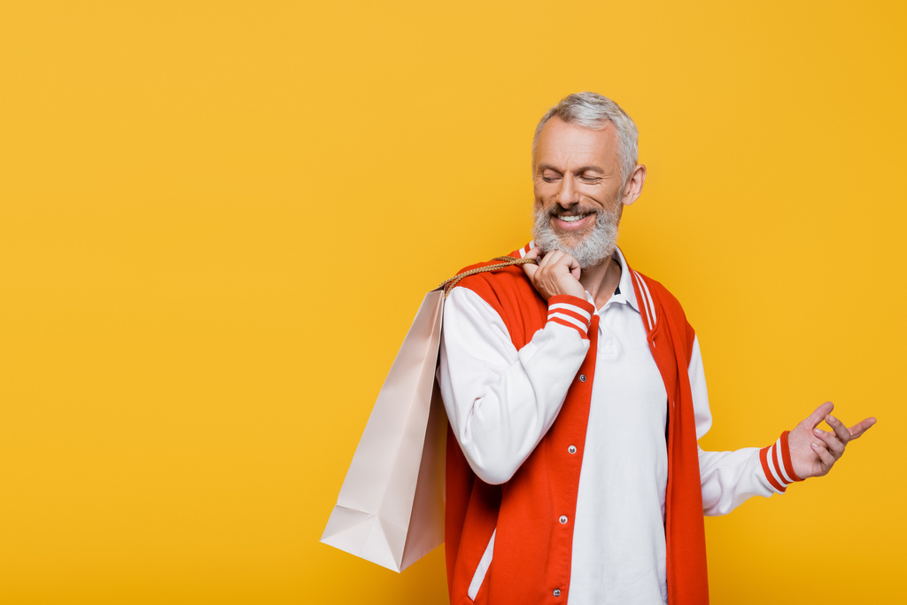 glücklicher Mann mittleren Alters in Bomberjacke mit Einkaufstasche in Gelb - Foto, Bild