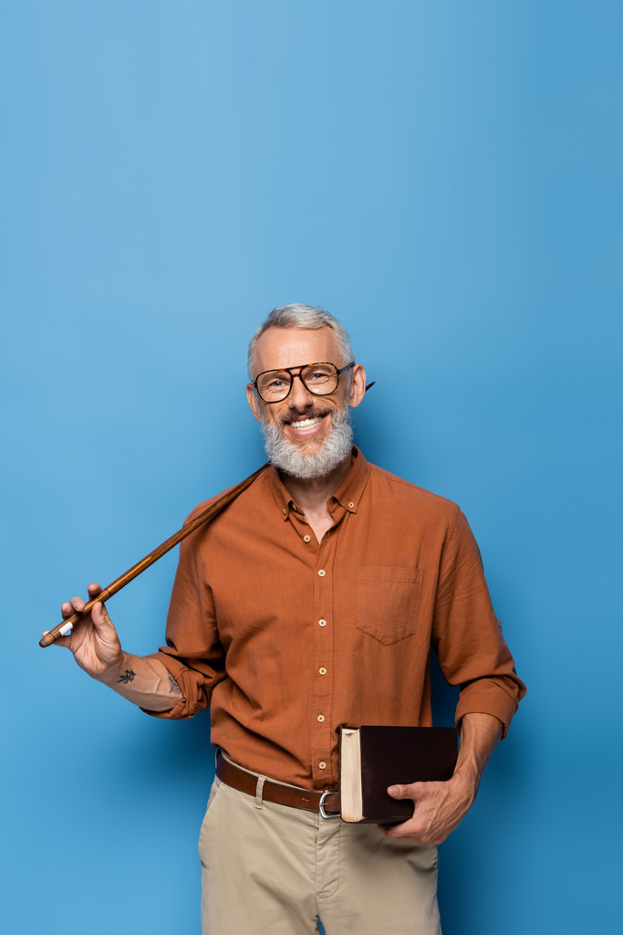 szczęśliwy nauczyciel w średnim wieku w okularach trzymając kij wskaźnik i książki na niebiesko - Zdjęcie, obraz