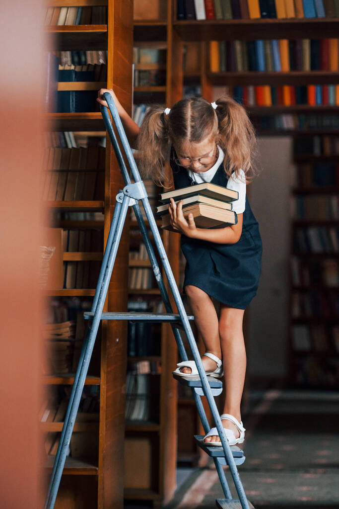 Шкільна дівчина на сходах у бібліотеці, повній книг. Концепція освіти
. - Фото, зображення