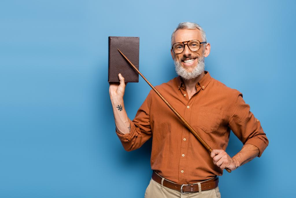 щасливий вчитель середнього віку в окулярах тримає вказівник палицю біля книги на синьому
 - Фото, зображення