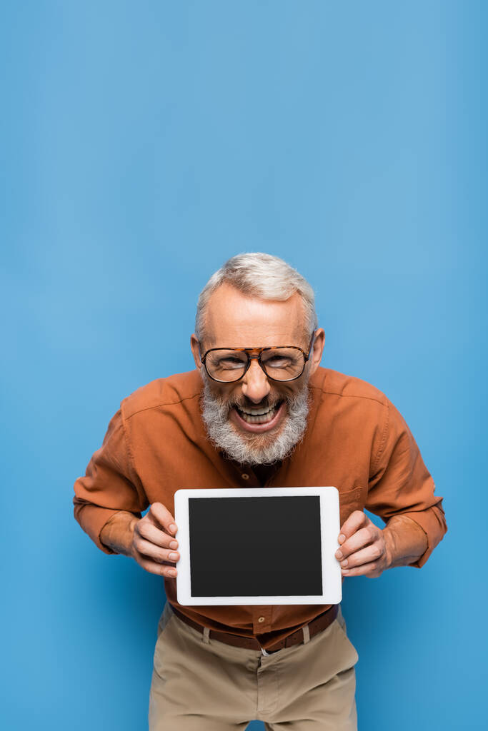 mosolygós középkorú férfi szemüvegben és ing tartja digitális tabletta üres képernyő kék - Fotó, kép