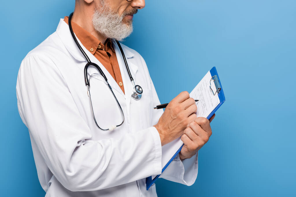 обрезанный вид врача средних лет в белом халате, выписывающего рецепт на планшете на синий - Фото, изображение