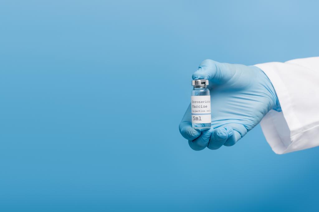 bijgesneden zicht op arts in latex handschoen met flacon met coronavirusvaccin geïsoleerd op blauw - Foto, afbeelding