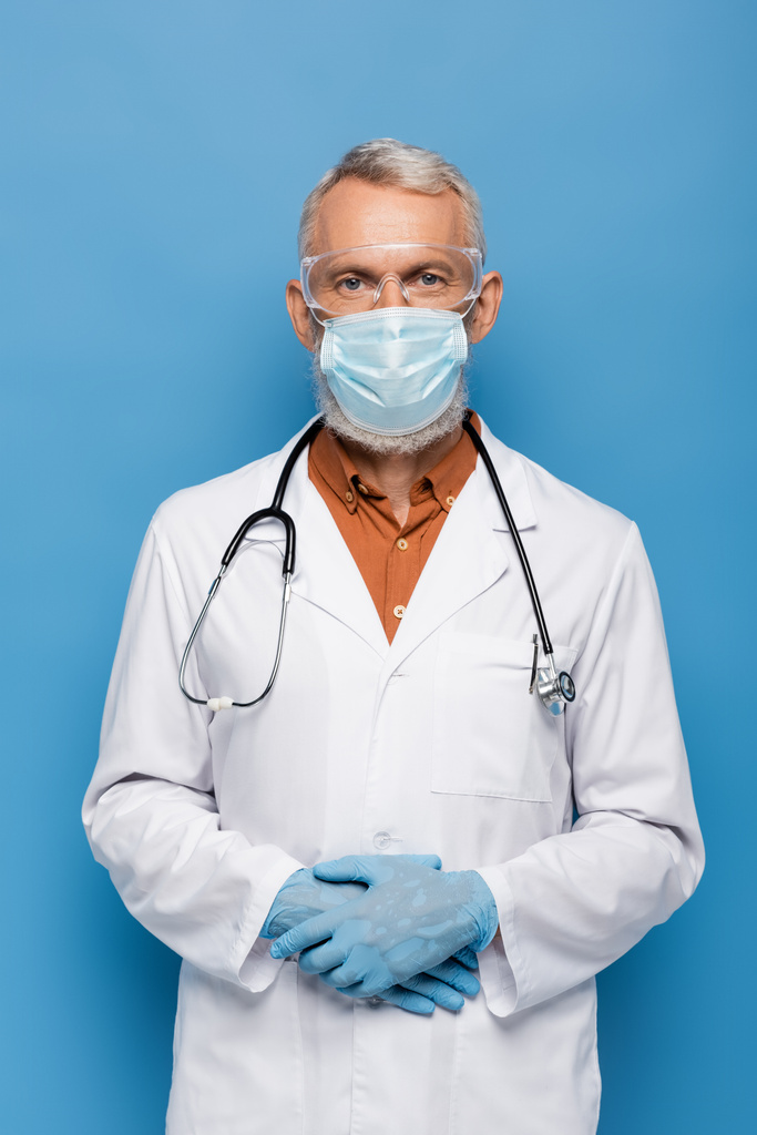 青の上に立つ白衣の中年医師医療用マスクとゴーグル - 写真・画像