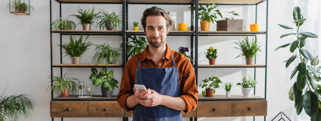Florist holding smartphone and looking at camera in flower shop, banner  - Photo, Image