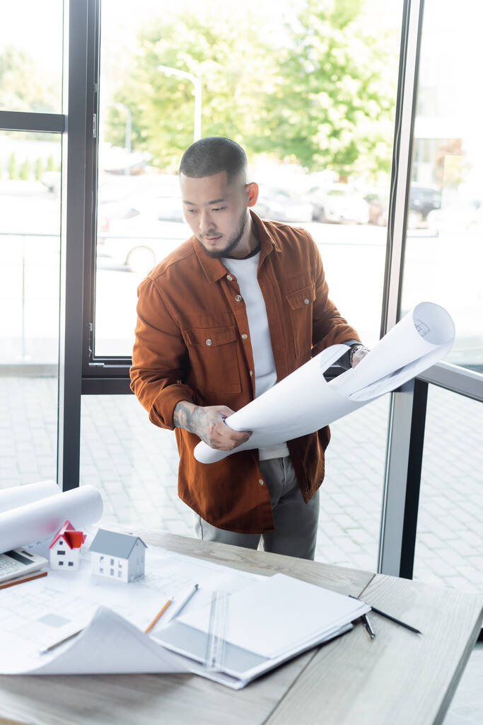 азиатский архитектор, глядя на документы на рабочем столе во время проведения чертежа в офисе - Фото, изображение