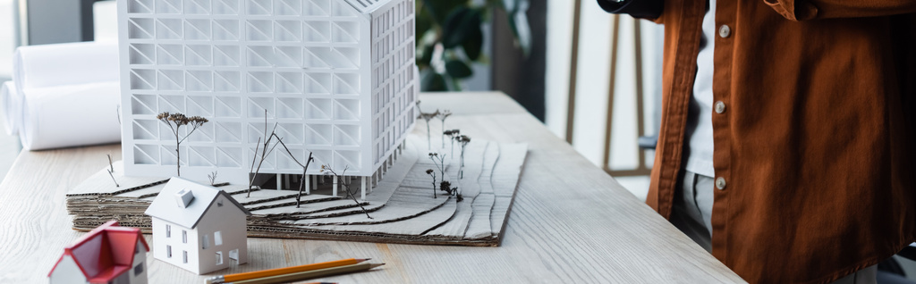 vista parziale di architetto in piedi vicino a modelli di casa sulla scrivania in ufficio, banner - Foto, immagini