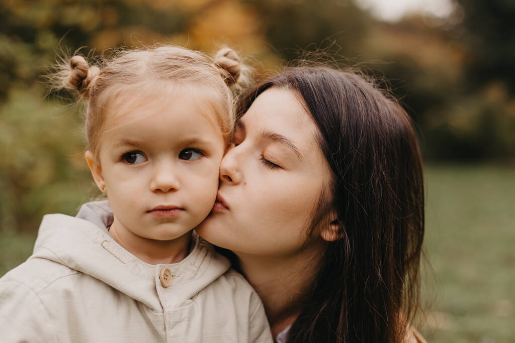 Fiatal boldog és mosolygós anya a kislányával a karjában ölelkezve és csókolózva eltölt egy hétvégét egy sétára az őszi parkban. szelektív fókusz, zajhatás, őszi hangulat - Fotó, kép