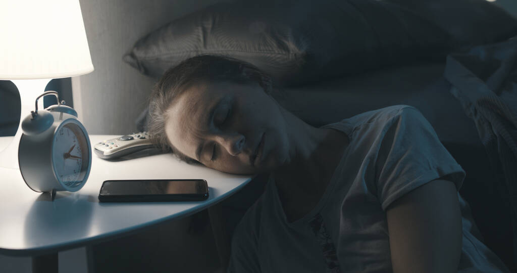 Uitgeputte vrouw ligt haar hoofd op het nachtkastje en slaapt 's nachts uit - Foto, afbeelding