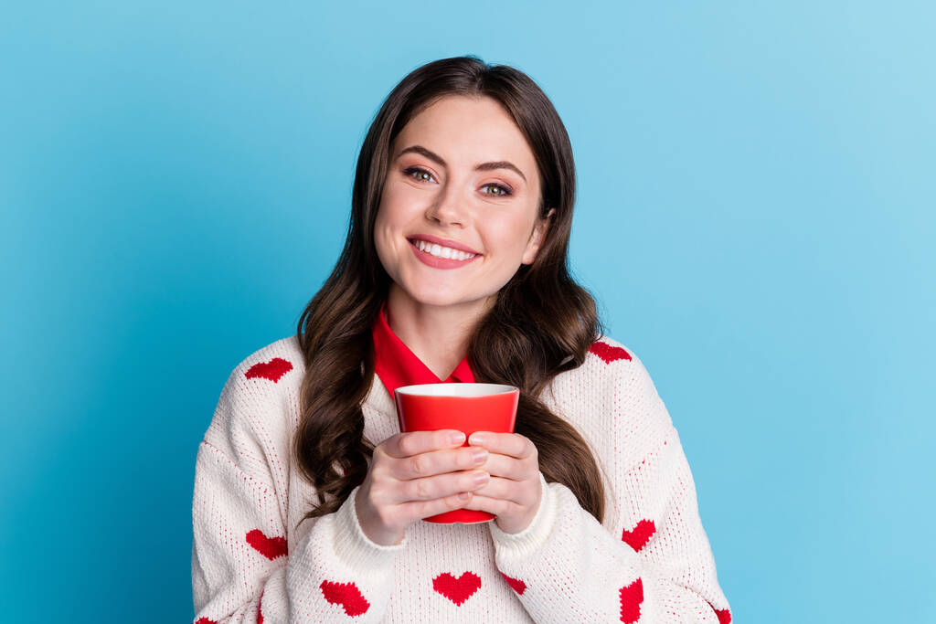 Fénykép a csinos bájos fiatal nő öltözött szív nyomtatás pulóver gazdaság piros csésze illatos kávé elszigetelt kék szín háttér - Fotó, kép