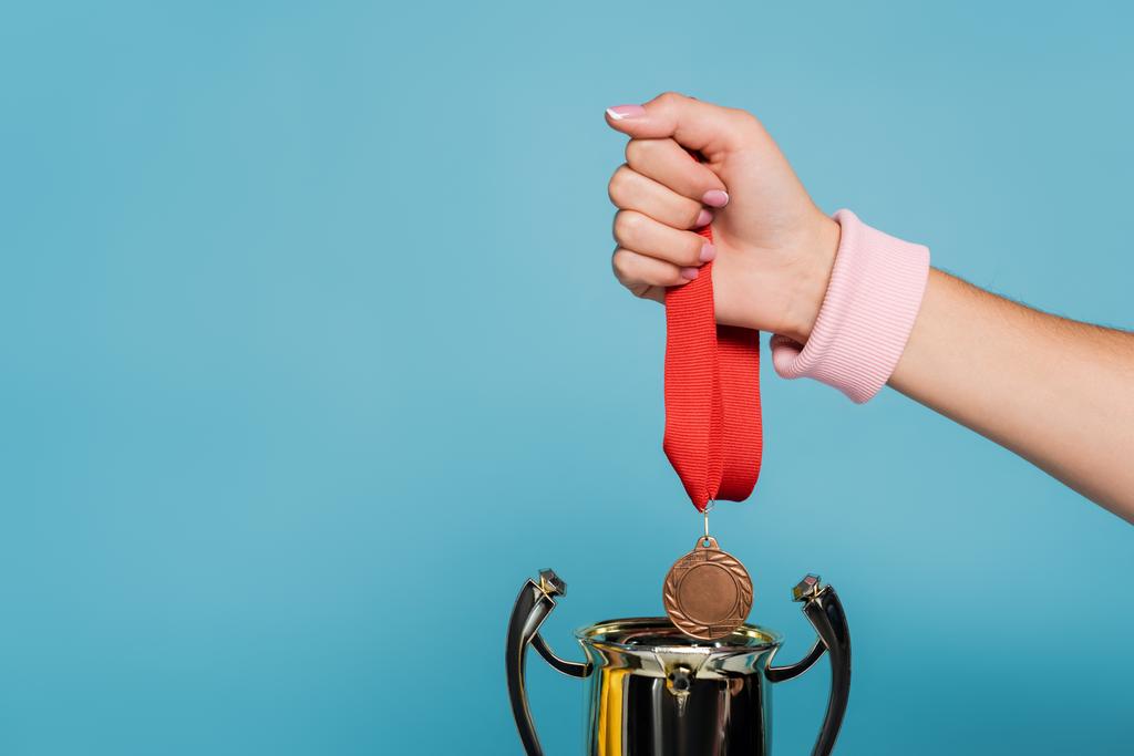 abgeschnittene Ansicht einer Sportlerin mit Medaille in der Nähe des goldenen Pokals isoliert auf blau - Foto, Bild