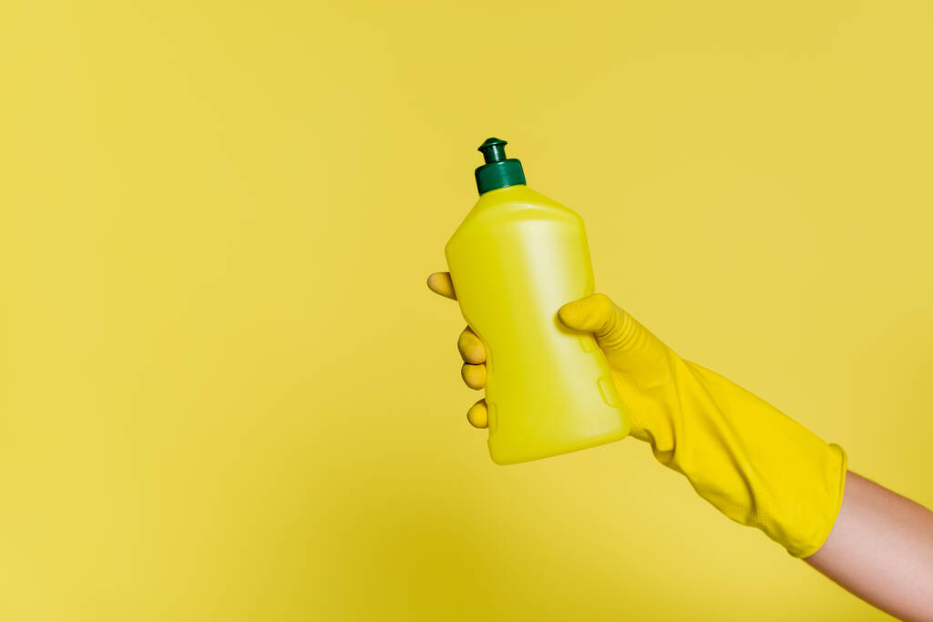 vista parziale di detergente in gomma guanto tenuta bottiglia con detergente su giallo - Foto, immagini