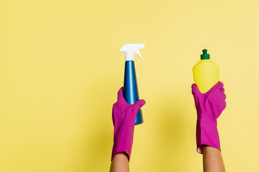 a tisztítószer részleges nézete a mosó- és tisztítószert tartó gumikesztyűben és a sárga flakon spray-ben - Fotó, kép