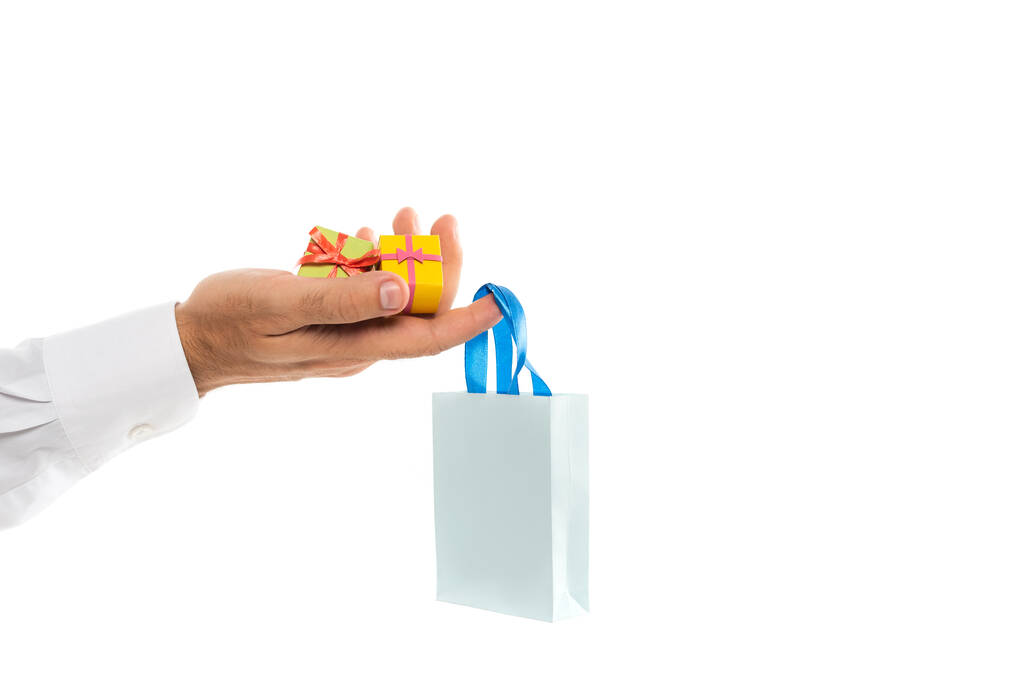 καλλιεργημένη άποψη του ανθρώπου κρατώντας χάρτινη σακούλα και μικροσκοπικά κουτιά δώρων που απομονώνονται σε λευκό  - Φωτογραφία, εικόνα
