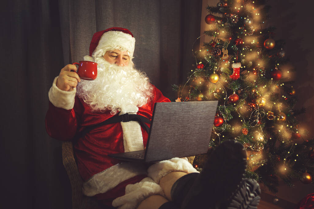 Hiteles Mikulás egy laptopon dolgozik. Otthoni. Karácsonyra és szilveszterre várva.  - Fotó, kép