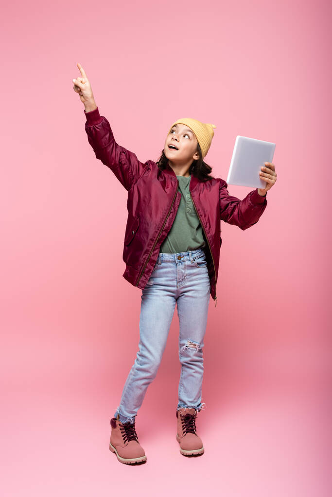 teljes hossza stílusos tizenéves lány gazdaság digitális tabletta és ujjal a rózsaszín  - Fotó, kép