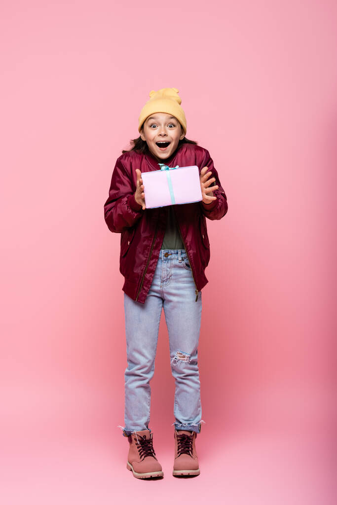 plná délka užaslé předpuberťačky v zimním oblečení držení zabalené dárek na růžové  - Fotografie, Obrázek