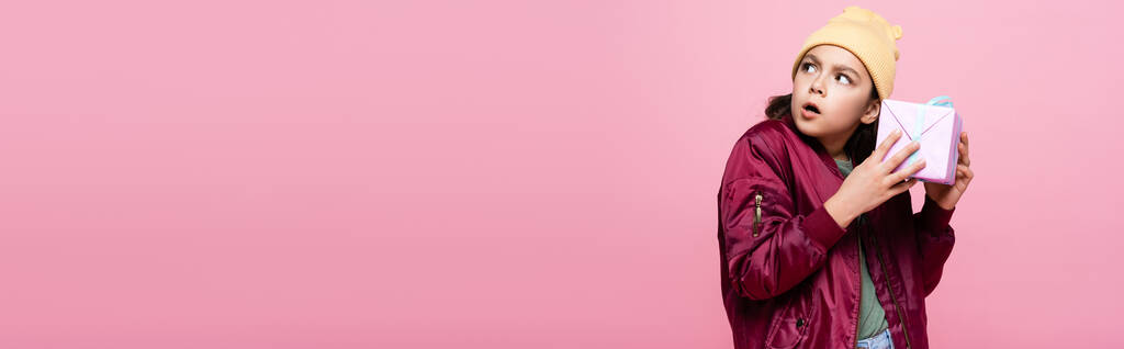 περίεργος preteen κορίτσι στο μοντέρνο ντύσιμο εκμετάλλευση τυλιγμένο παρόν απομονώνονται σε ροζ, πανό - Φωτογραφία, εικόνα