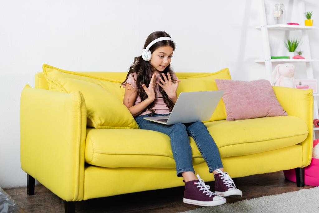 menina pré-adolescente em fones de ouvido sem fio falando durante a chamada de vídeo enquanto estuda on-line em casa - Foto, Imagem