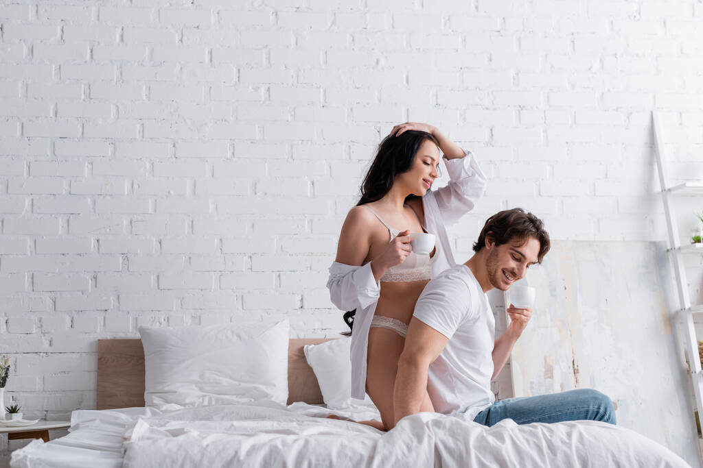 sexy junges Paar lächelt beim morgendlichen Kaffee im Schlafzimmer - Foto, Bild