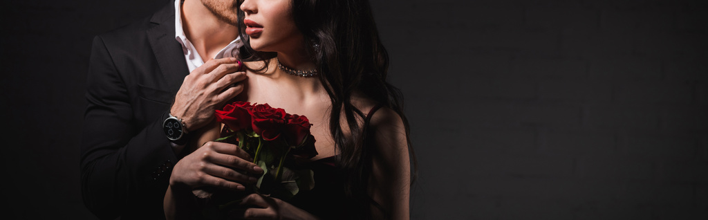 περικοπή άποψη του άνδρα συγκινητικό ώμο της γυναίκας με κόκκινα τριαντάφυλλα σε σκούρο φόντο, λάβαρο - Φωτογραφία, εικόνα