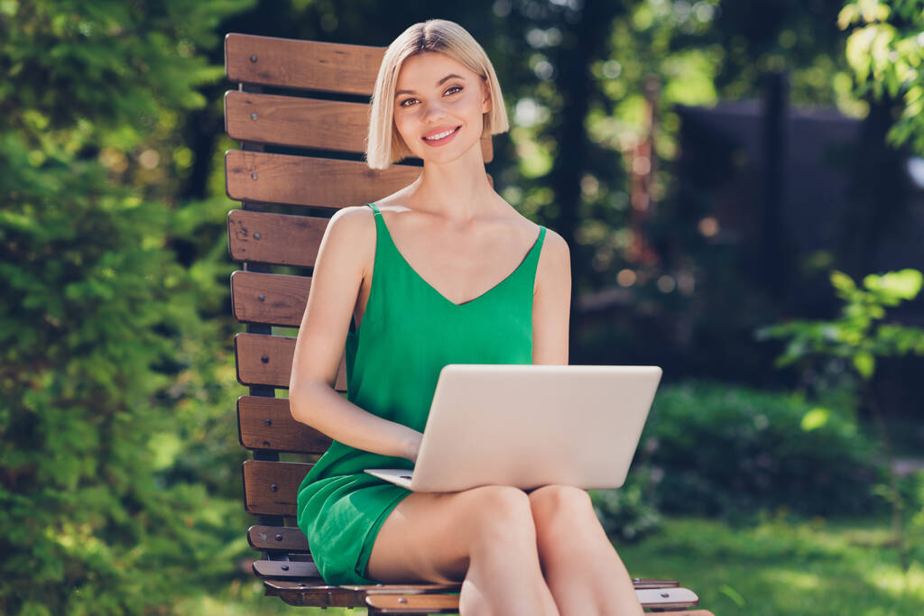 甘いかなり若い女性の写真緑の服を着てベンチに座って働く現代的なデバイスは、都市の通りの外で笑顔 - 写真・画像
