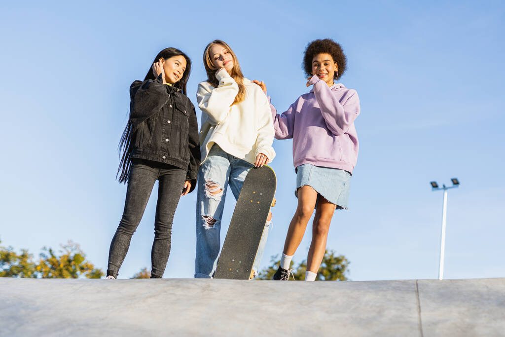 Wielokulturowa grupa młodych przyjaciół nawiązujących więź na świeżym powietrzu i bawiących się - stylowe, chłodne nastolatki zbierające się w miejskim skateparku - Zdjęcie, obraz