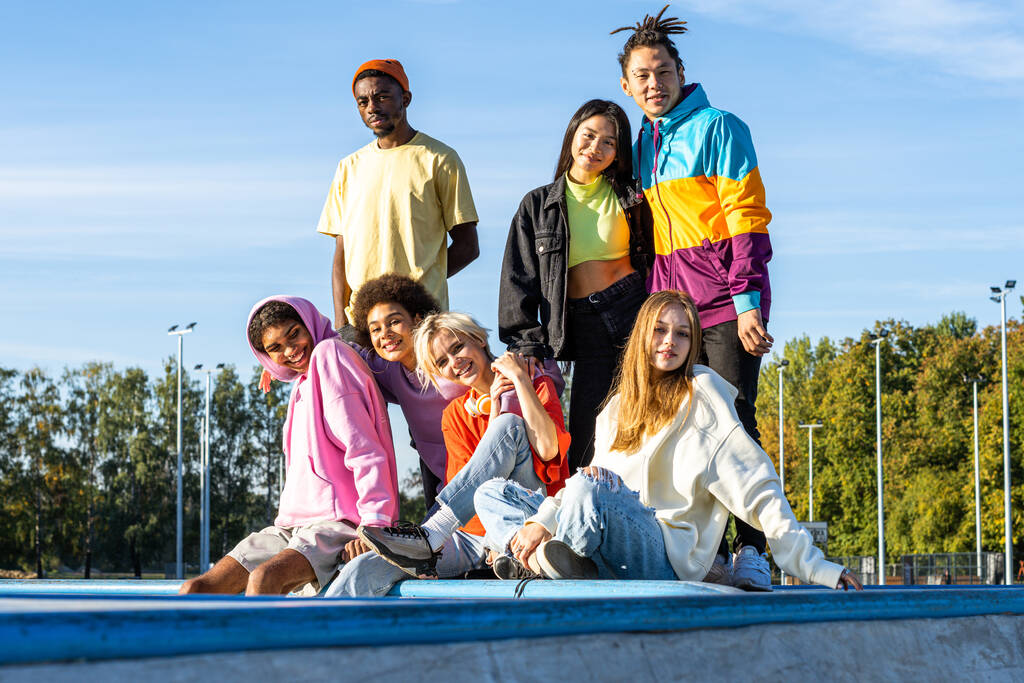 Grupo multicultural de jóvenes amigos que se unen al aire libre y se divierten - Adolescentes cool con estilo que se reúnen en el parque de skate urbano - Foto, imagen
