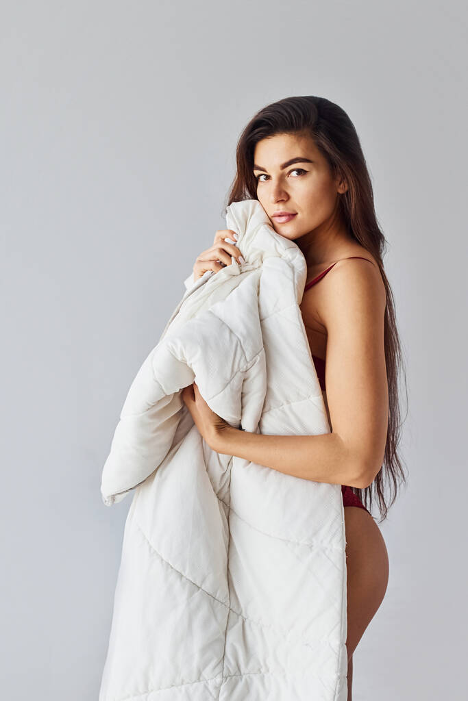 Frau bedeckt ihren Körper mit Handtuch im Studio vor weißem Hintergrund. - Foto, Bild
