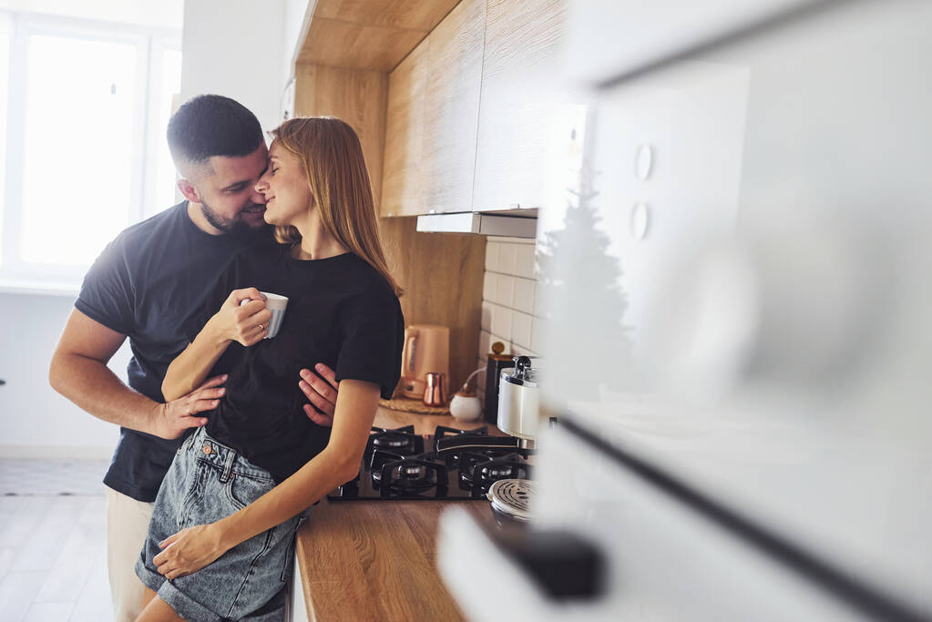 With cup of fresh drink. Morning for young married couple that standing indoors in the kitchen. - Photo, Image