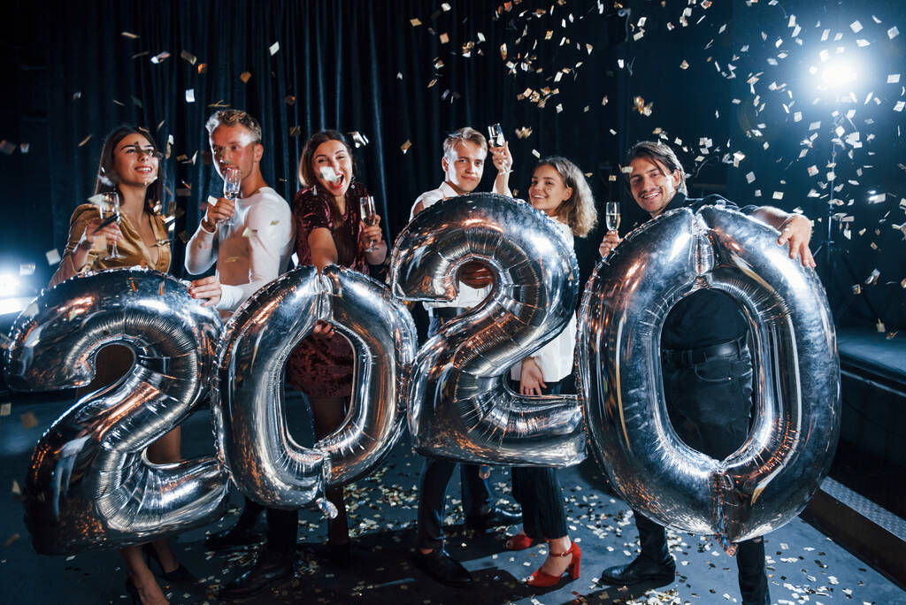 Konfetti liegt in der Luft. Fröhliche Gruppe von Menschen mit Getränken und Luftballons in den Händen feiert das neue Jahr 2020. - Foto, Bild