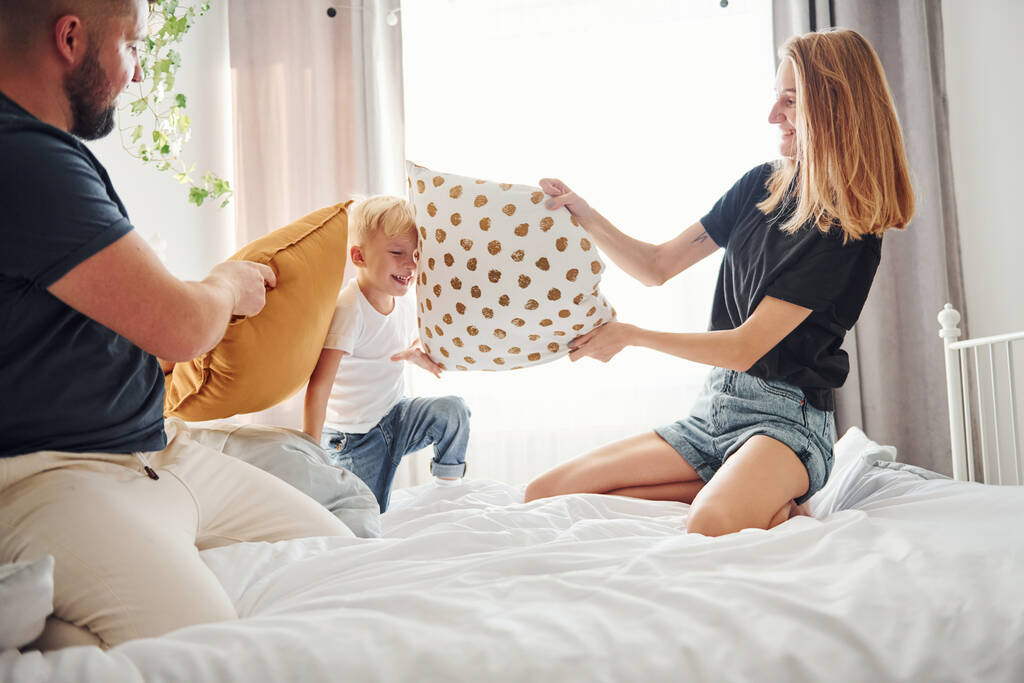 Genç evli çift ve küçük oğulları gündüz yatak odasında yastık savaşı yapıyorlar.. - Fotoğraf, Görsel