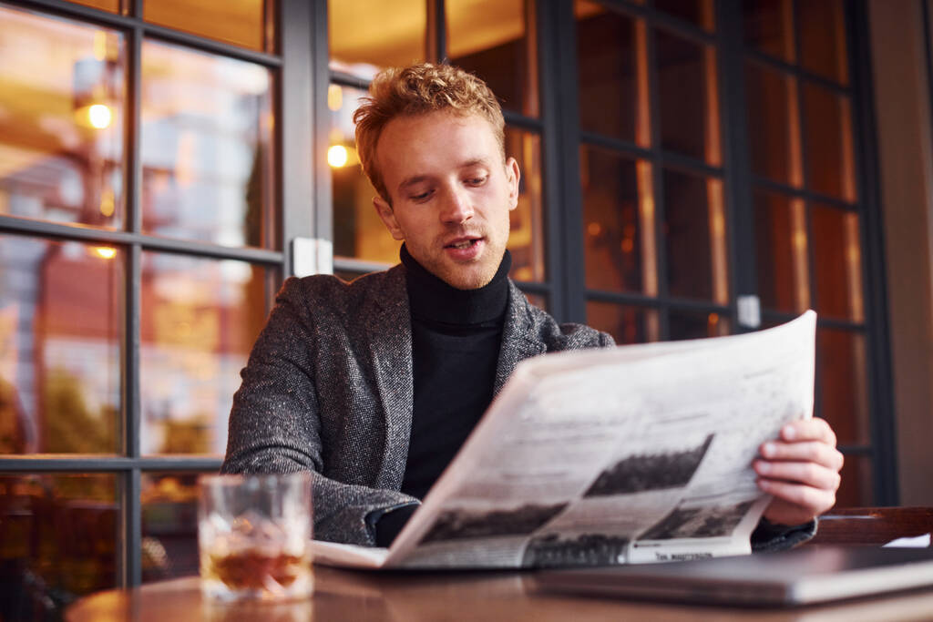 Retrato de un joven moderno con ropa formal que se sienta en la cafetería y lee el periódico. - Foto, imagen