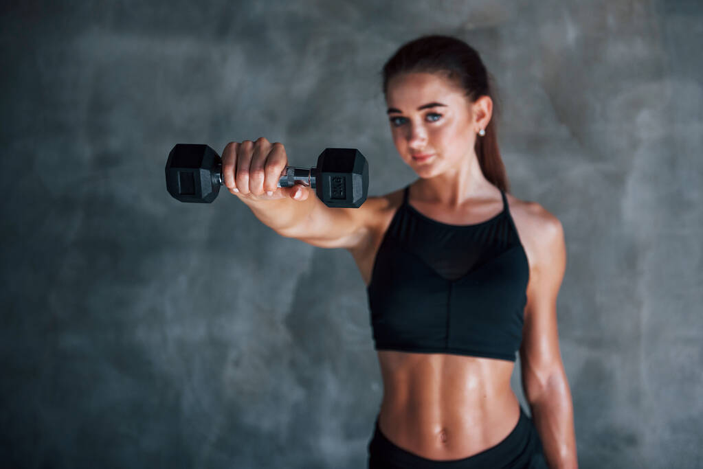 Jeune femme de fitness est dans la salle de gym près du mur avec haltères dans les mains. - Photo, image