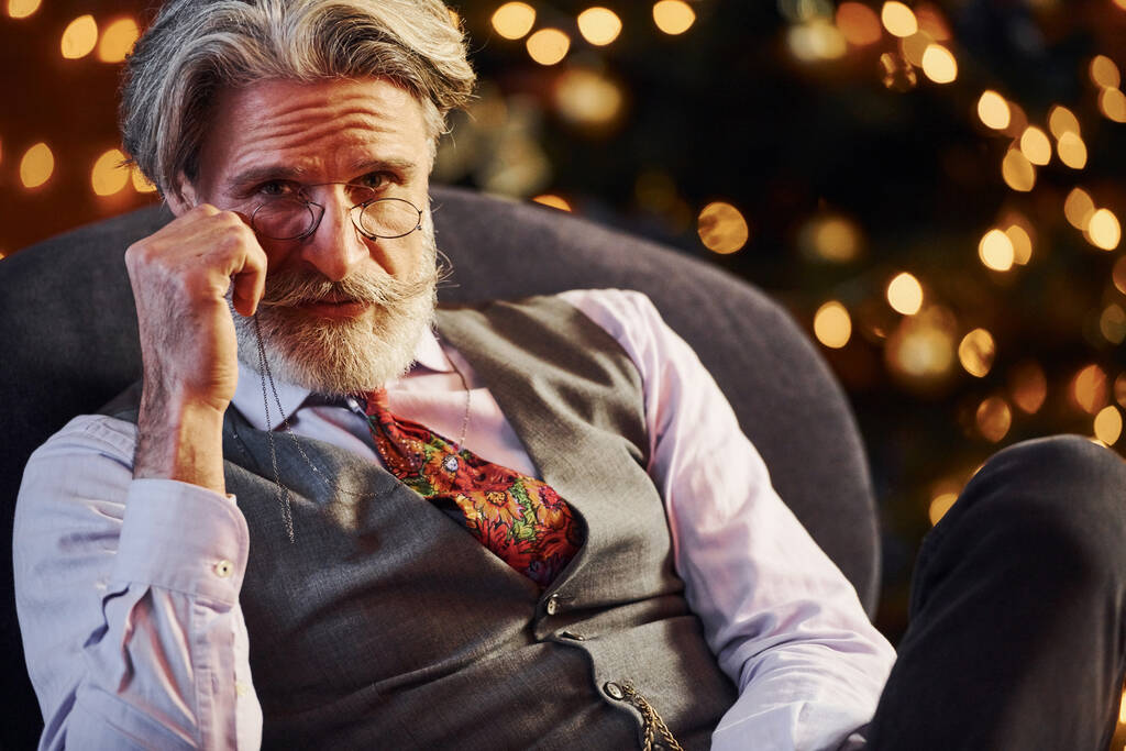 Ritratto di anziano elegante con capelli grigi e barba è in camera decorata Natale seduto sulla sedia. - Foto, immagini