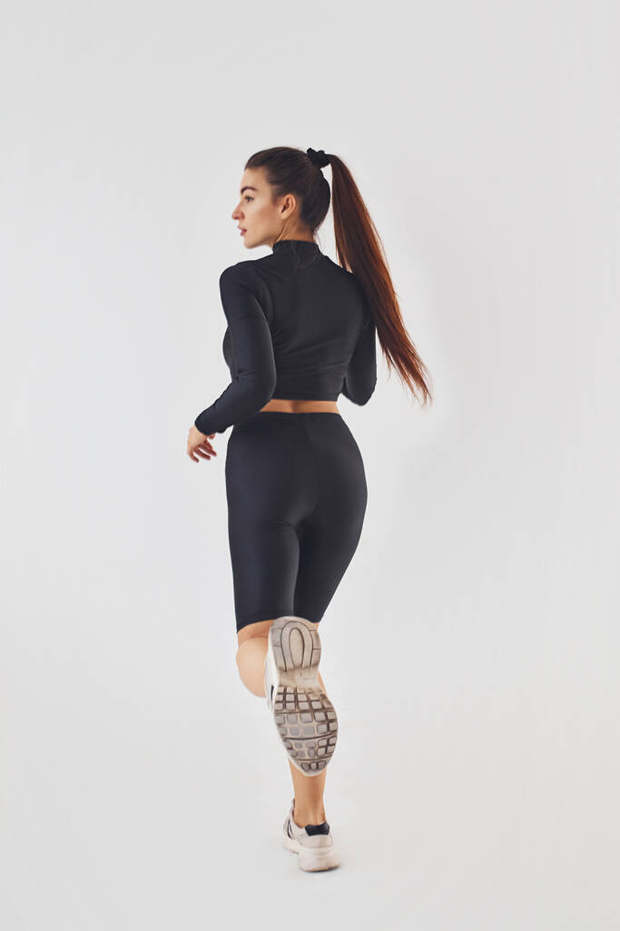 Спортивная женщина в черной одежде делает упражнения в студии на белом фоне. - Фото, изображение