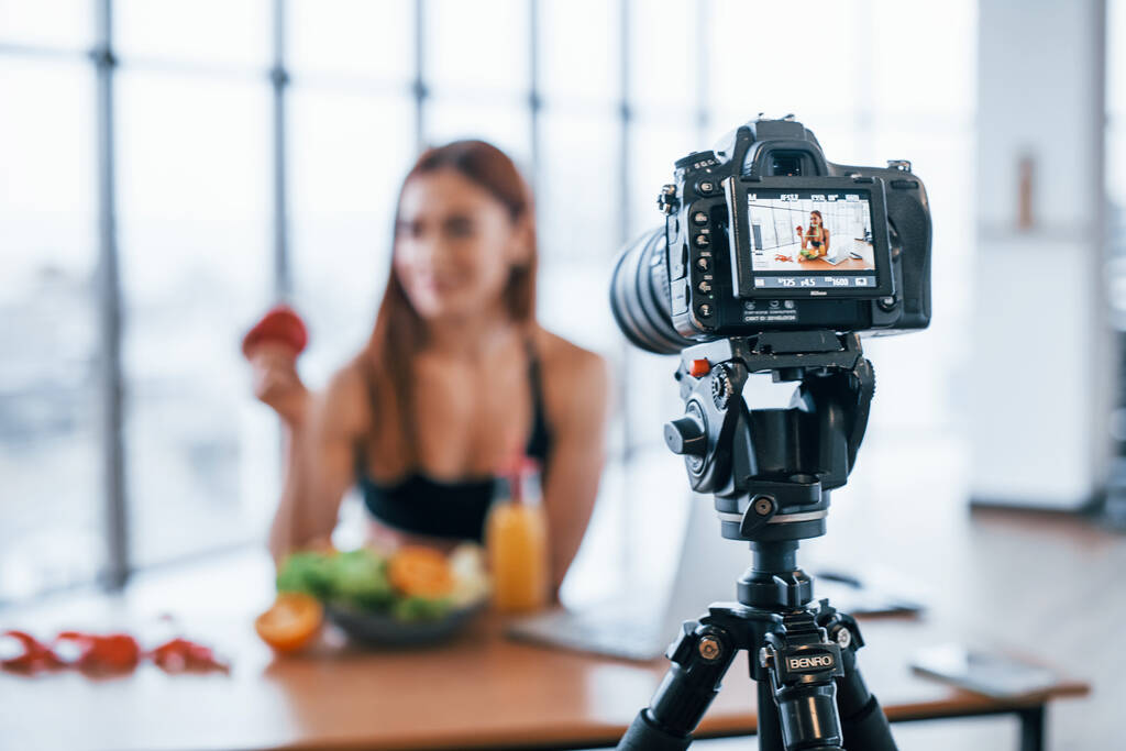 Vlogger femenina con cuerpo deportivo de pie en el interior cerca de la mesa con alimentos saludables. - Foto, Imagen