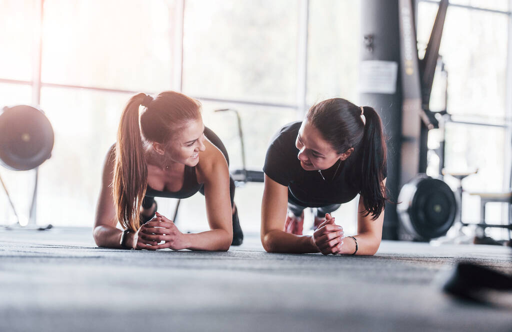 Dwie młode dziewczyny w sportowym ubraniu ćwiczą razem na siłowni.. - Zdjęcie, obraz