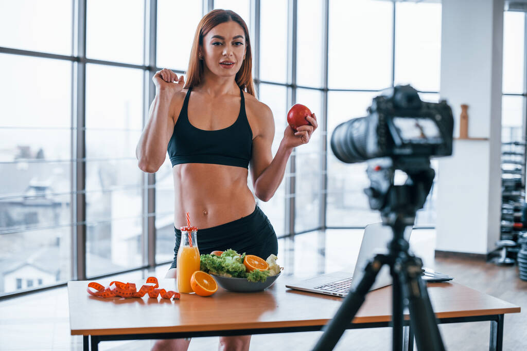 Női vlogger sportos test áll beltérben közelében asztal egészséges étel. - Fotó, kép