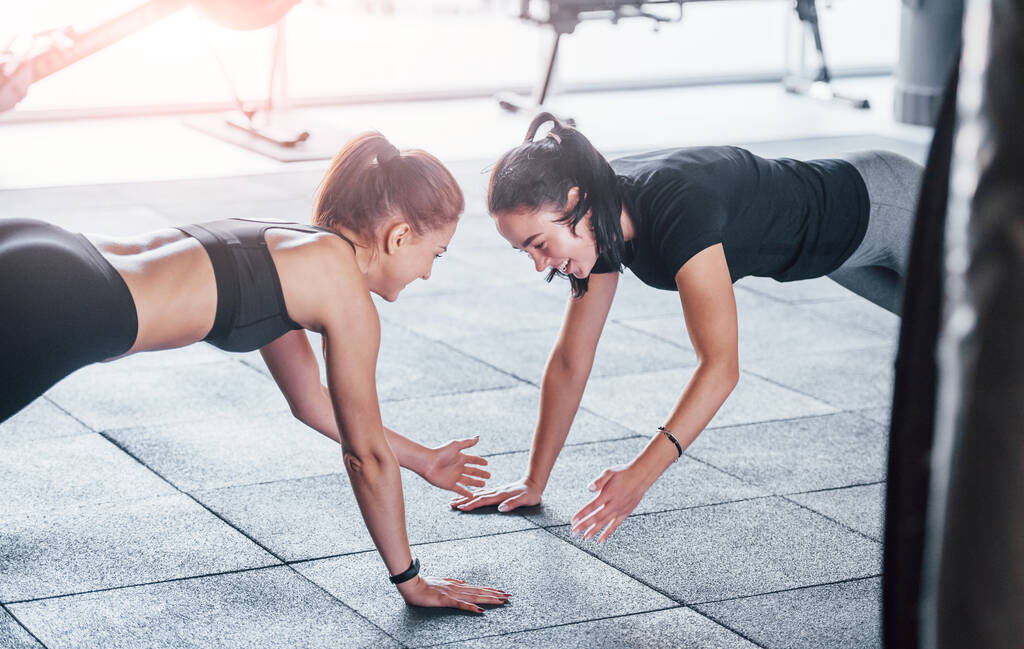 Deux jeunes filles en vêtements de sport est dans la salle de gym faire des exercices ensemble. - Photo, image