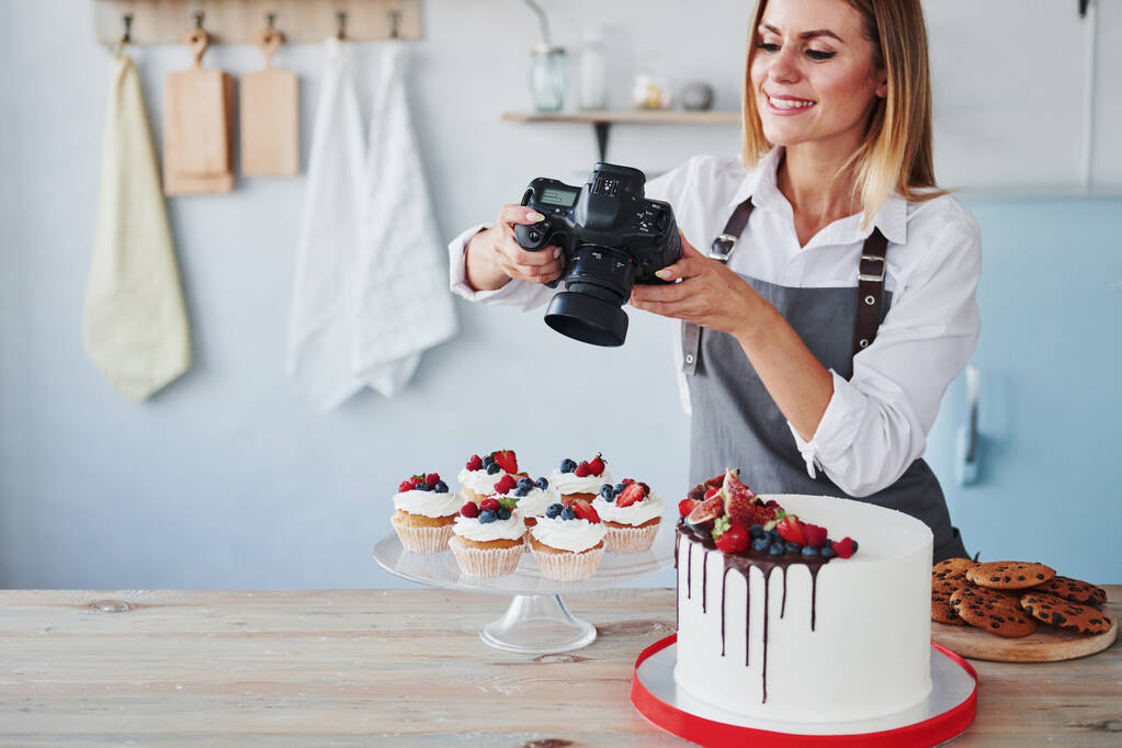 女性は台所に立って、カメラを使用して彼女の自家製のクッキーとパイの写真を撮る. - 写真・画像