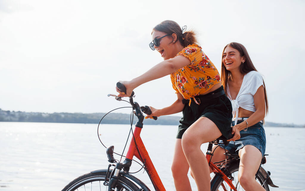 自転車に乗っている2人の女性の友人は湖の近くのビーチで楽しんでいます. - 写真・画像